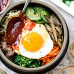 Bibimbap served with a sunny side up fried egg in an earthenware with a gochujang sauce on top