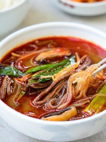 Korean red spicy soup with shredded beef, scallions, mushrooms and noodles in a large bowl