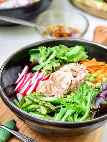 Bibimbap in a large dark color bowl with canned tuna on top with colorful spring vegetables