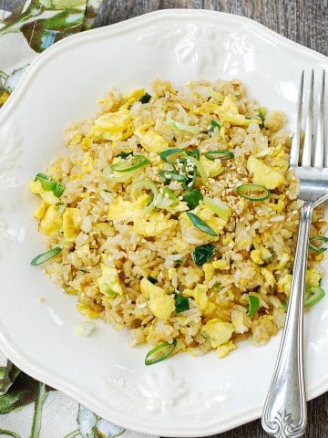 Egg fried rice with scallions in a white plate with a fork
